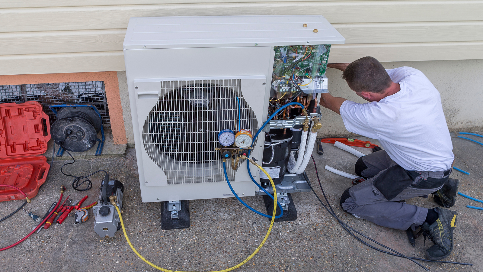 HVAC technician working on an outdoor air conditioning unit next to a house.