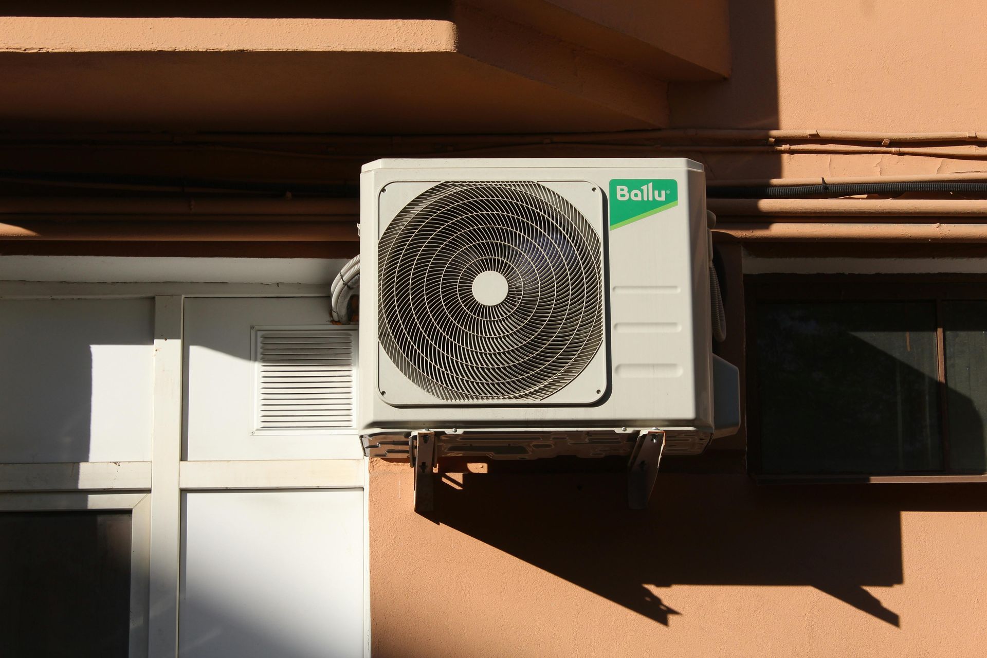 Air conditioning unit mounted on a peach-colored building wall.