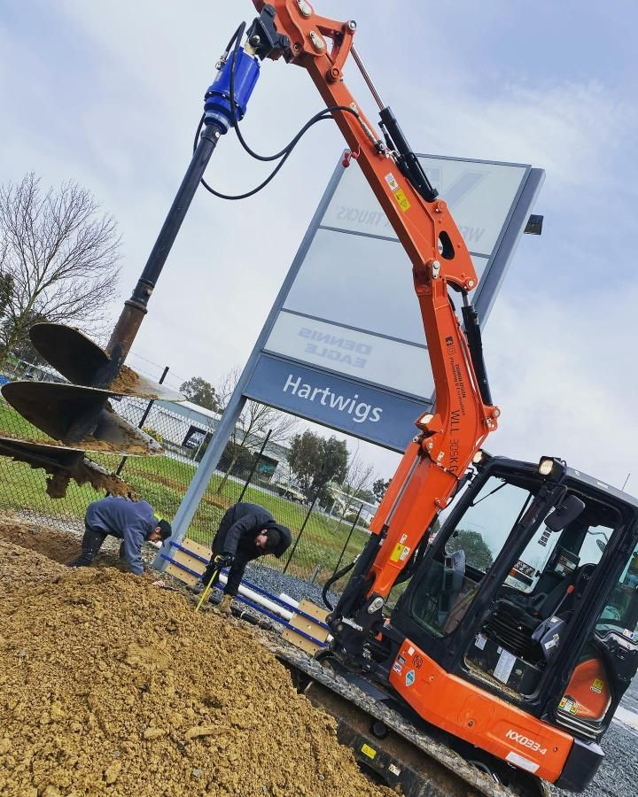 Man is Digging a Hole With a Machine in Front of a Sign That Says Hartwigs — Donaldson Plumbing & Excavations in Albury, VIC