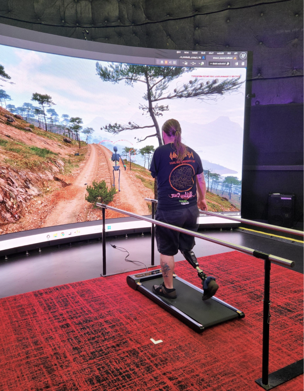 Person using a treadmill in a curved indoor VR running setup with a large scenic landscape display.