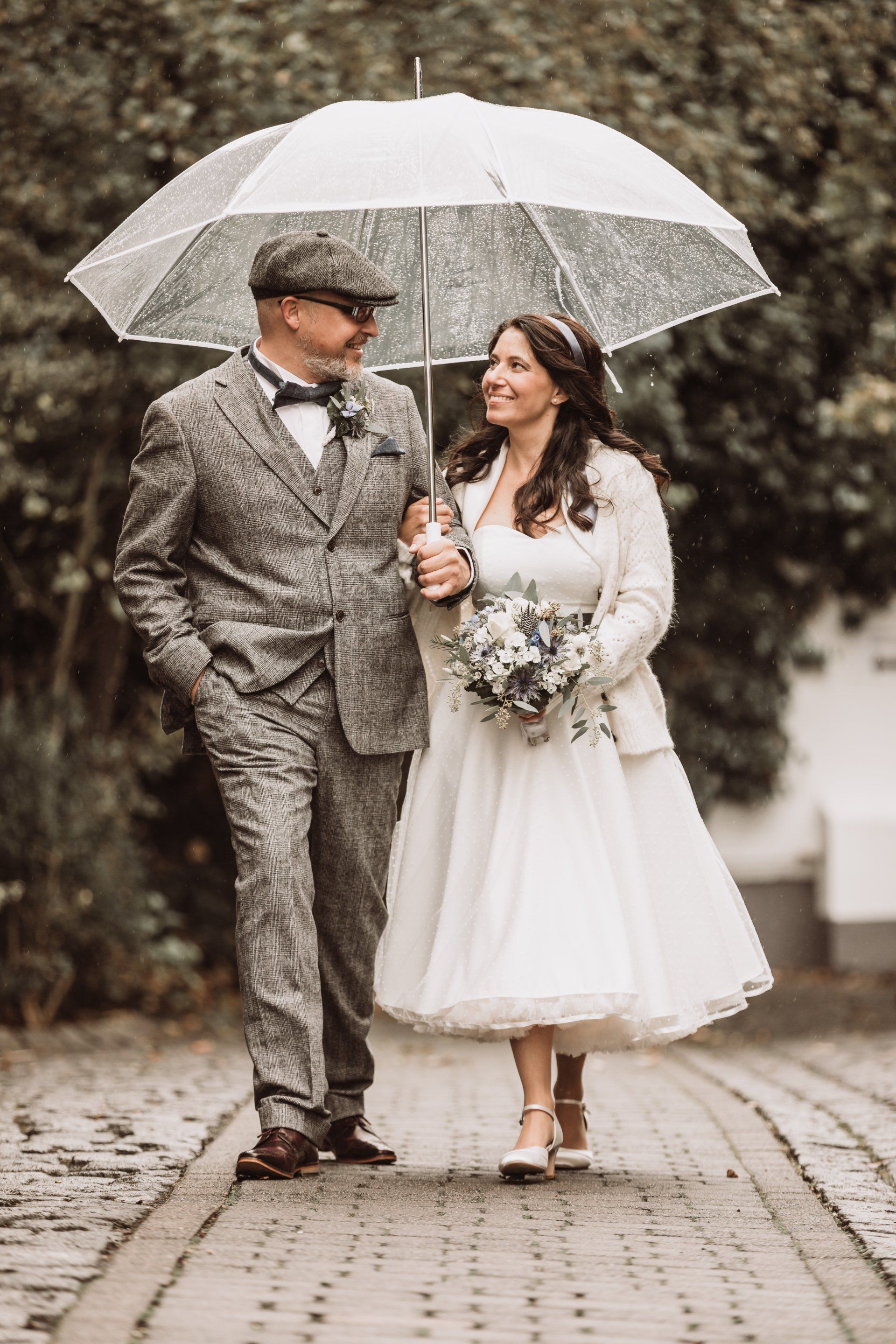 Eine Braut und ein Bräutigam gehen unter einem Regenschirm im Regen spazieren.