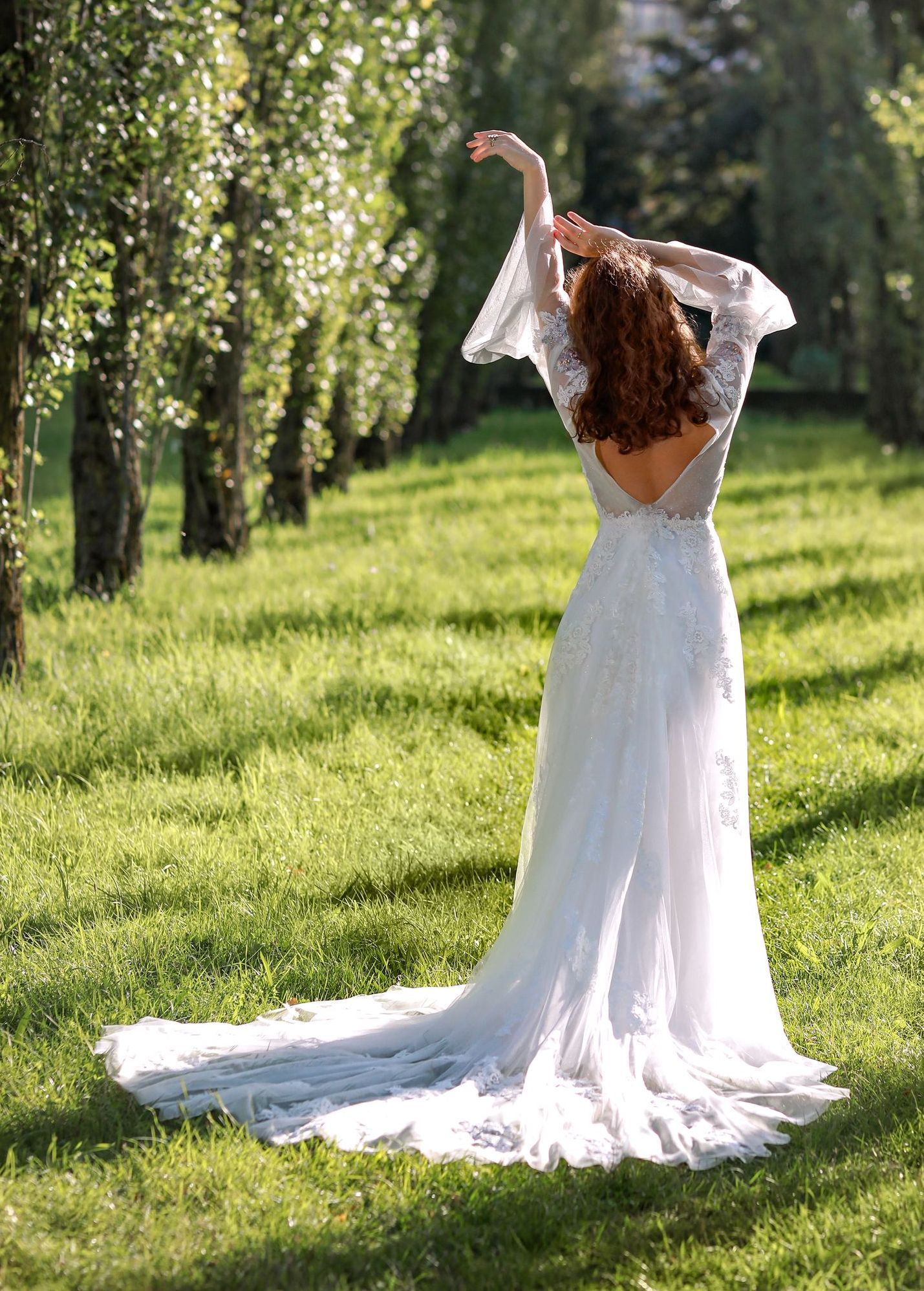 Eine Frau in einem Brautkleid steht mit ausgestreckten Armen auf einem Feld.