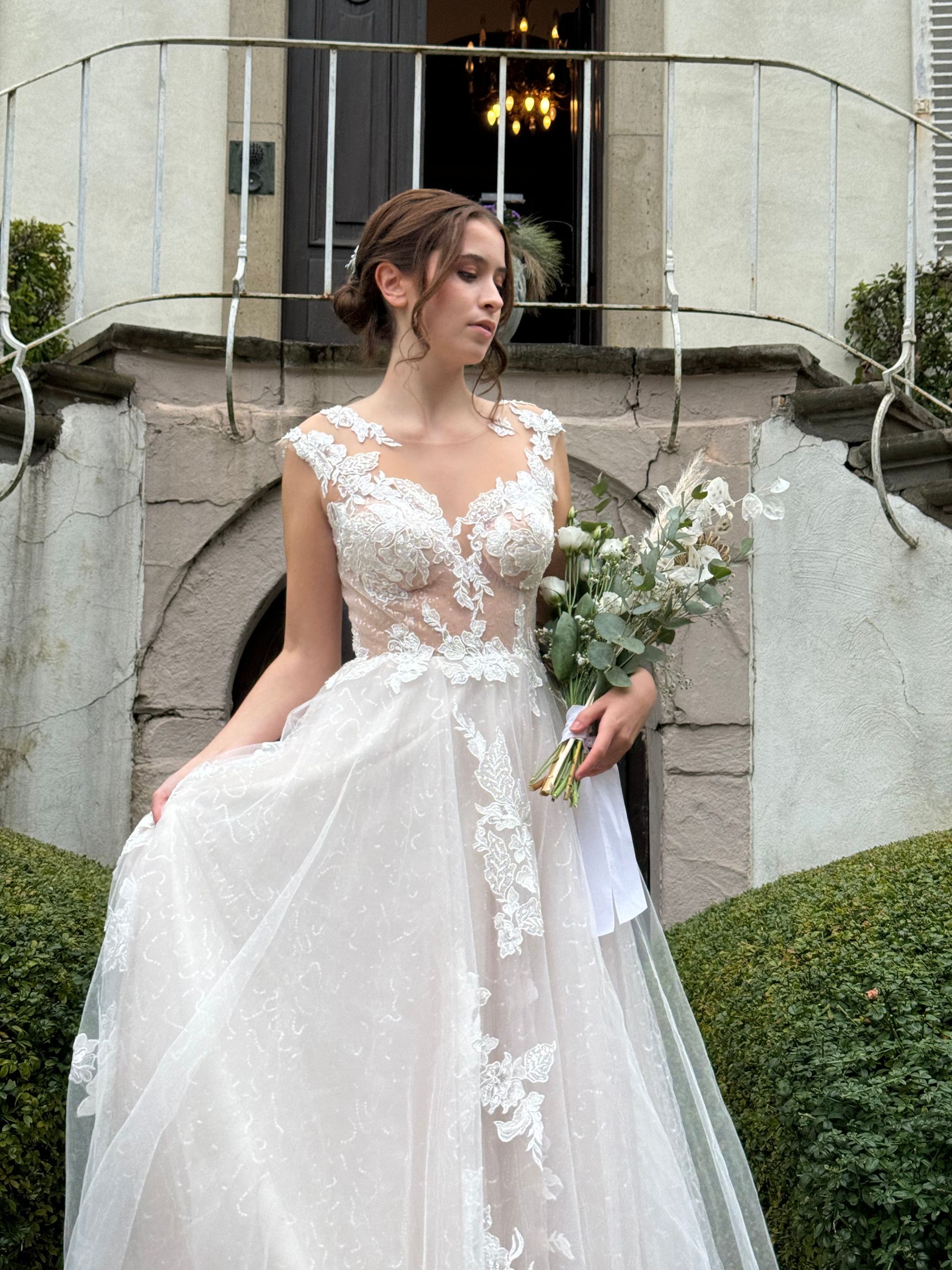 Eine Frau in einem Brautkleid hält einen Blumenstrauß vor einem Gebäude.