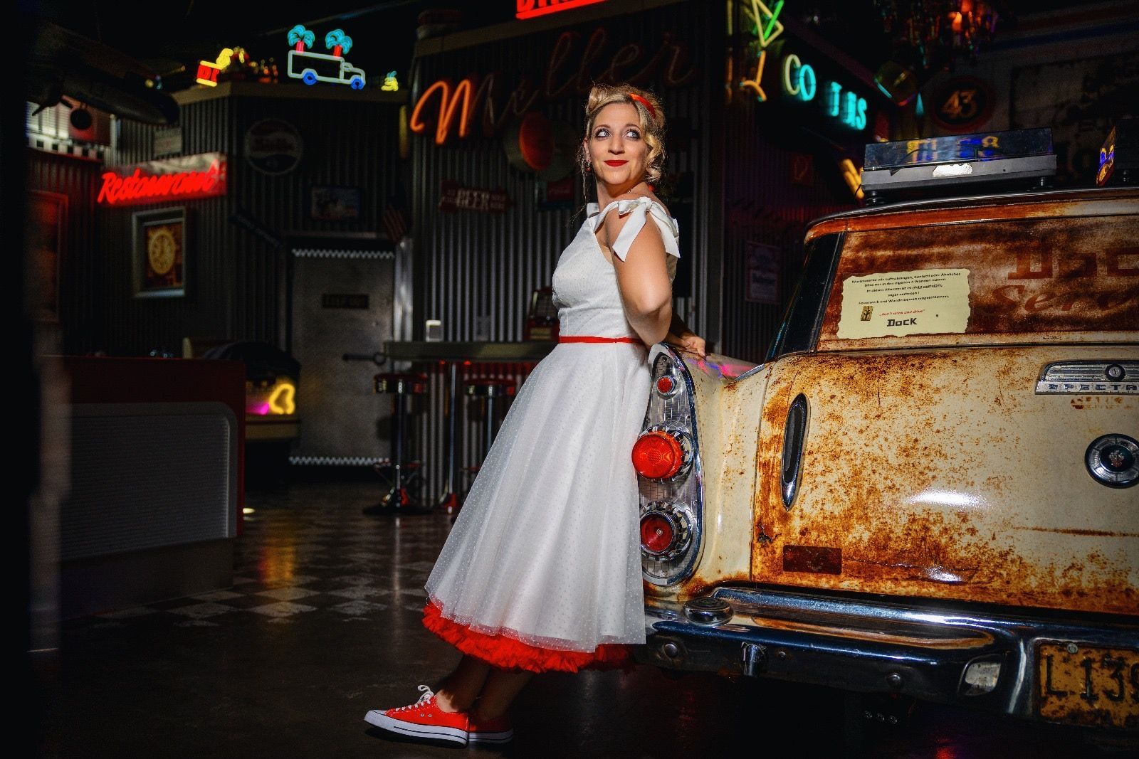 Eine Braut angelehnt an einem Oldtimer in einem Diner, in ihrem Rockabilly Hochzeitskleid.