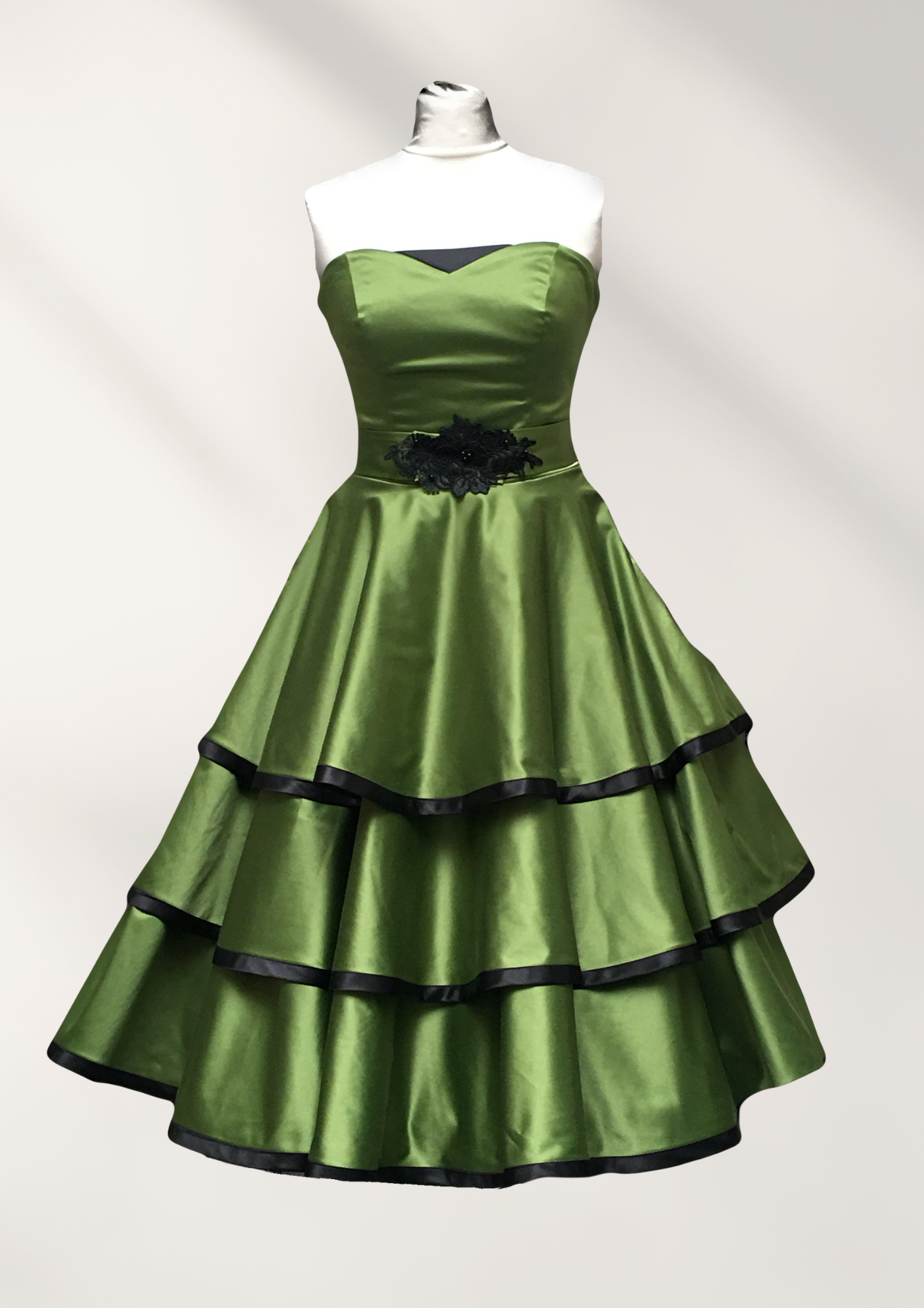 Ein grünes Kleid mit schwarzem Besatz hängt an einer Schaufensterpuppe