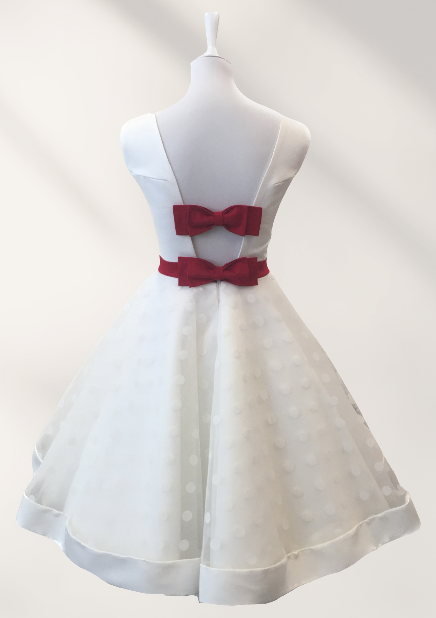 Auf einer Schaufensterpuppe hängt ein weißes Kleid mit einer roten Schleife auf dem Rücken.