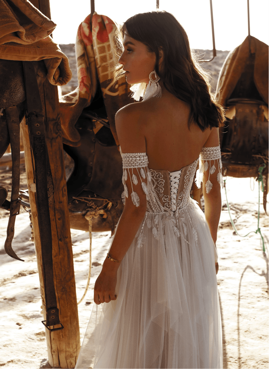 Eine Frau in einem Brautkleid steht neben einem Kamel am Strand.