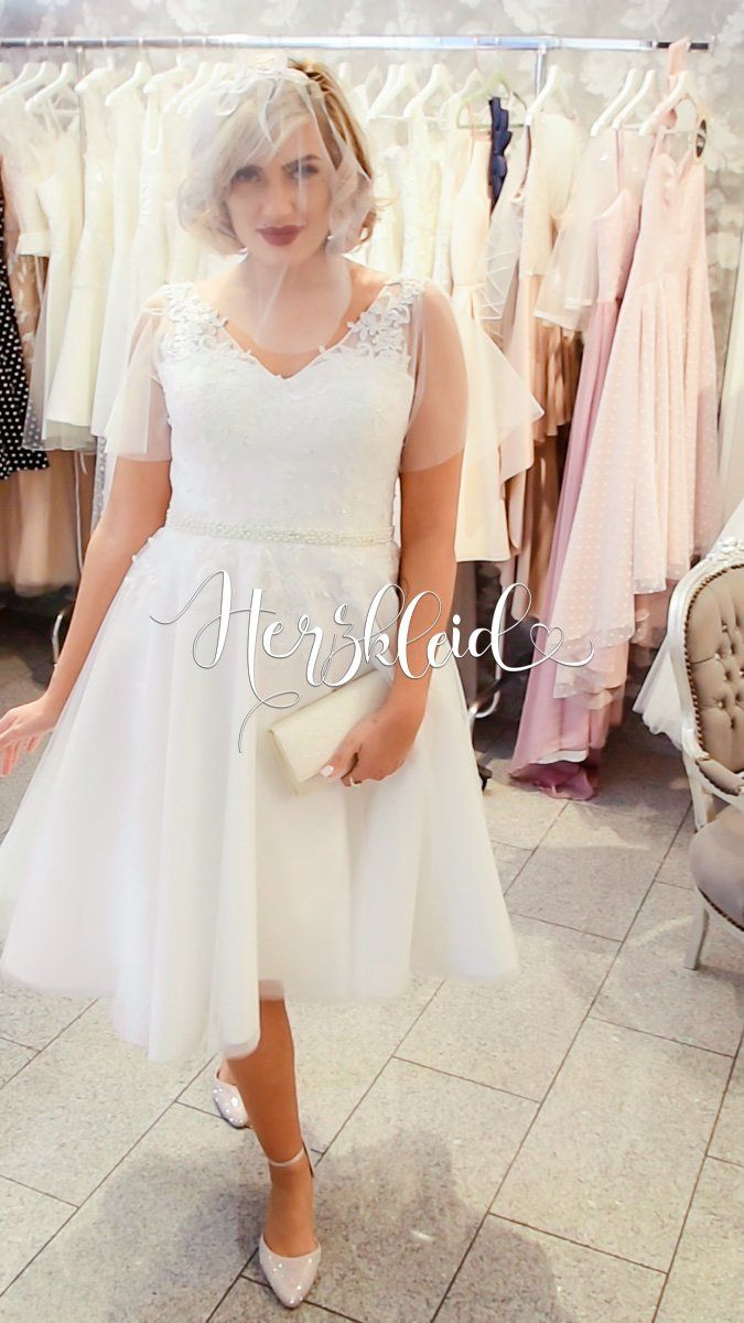 Eine Frau in einem weißen Kleid steht vor einem Kleiderständer.