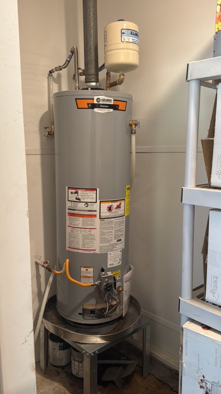 A tall, gray water heater with attached venting in a corner of a room, next to a shelf.