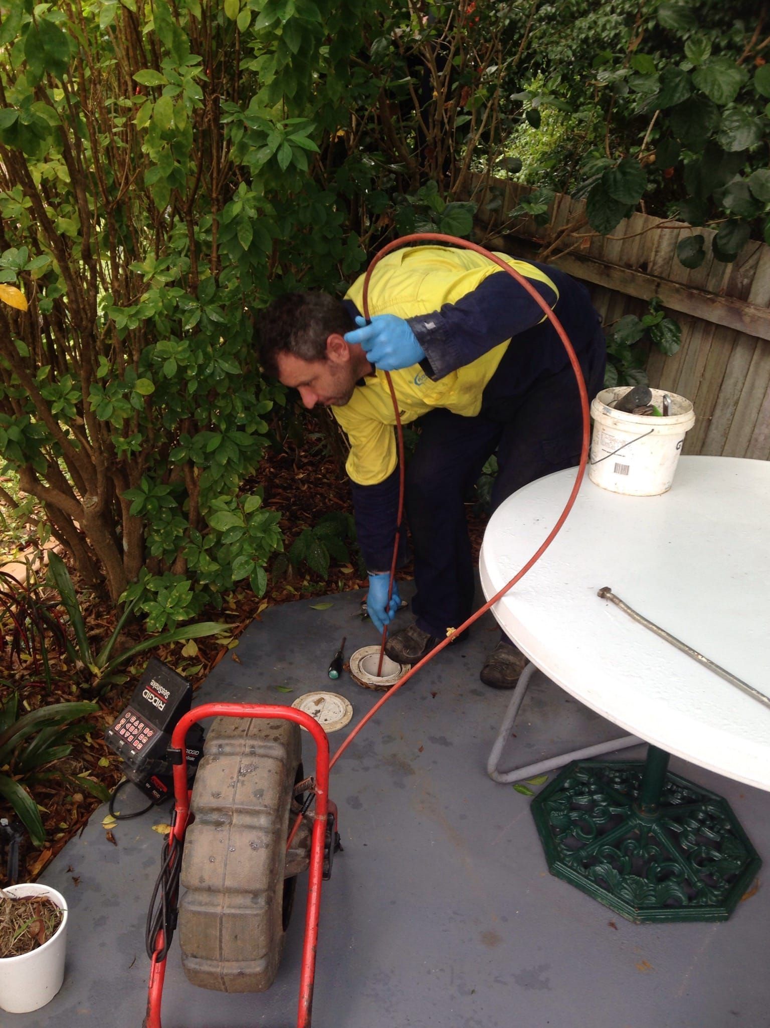A Man is Working on a Drain on a Patio Next to a Table — FlowWise in Maroochydore, QLD
