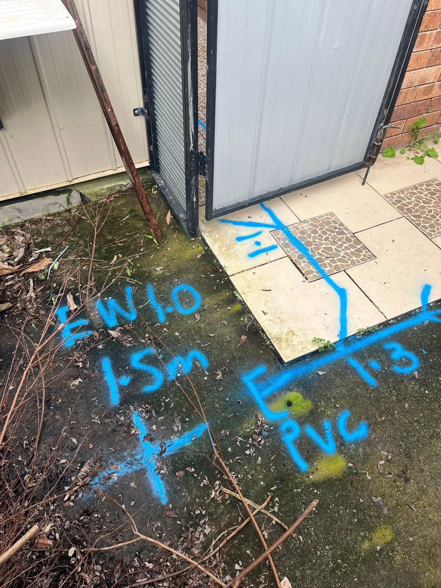 Blue Markings on Concrete Near a Gate, Indicating Underground PVC Pipe