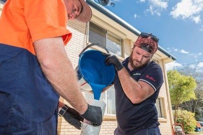 Two Men Are Pouring Blue Liquid Into a Bucket — FlowWise in Maroochydore, QLD
