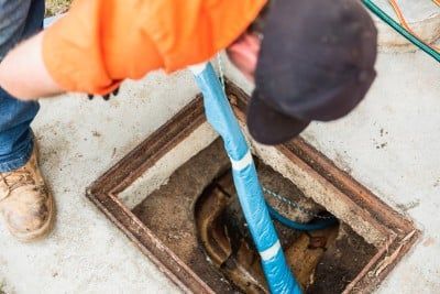 A Man is Cleaning a Manhole Cover With a Hose — FlowWise in Maroochydore, QLD