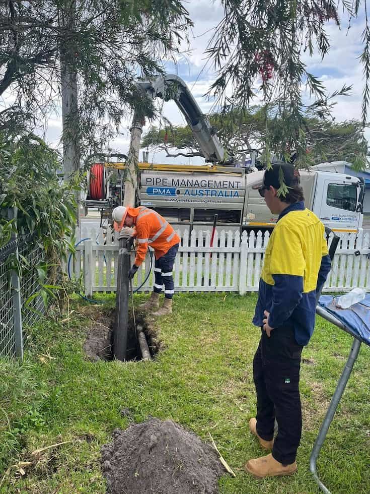 Two Workers in Safety Gear Operate Near a Trench in a Grassy Area