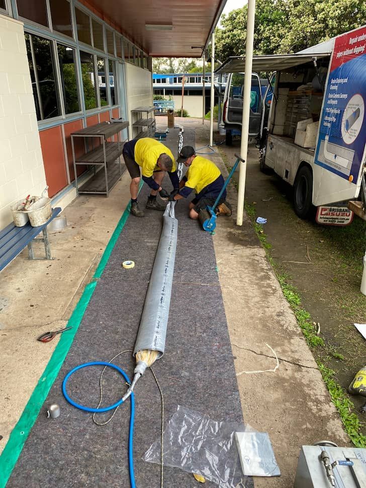 Two Workers in Yellow Shirts Install a Long Pipe