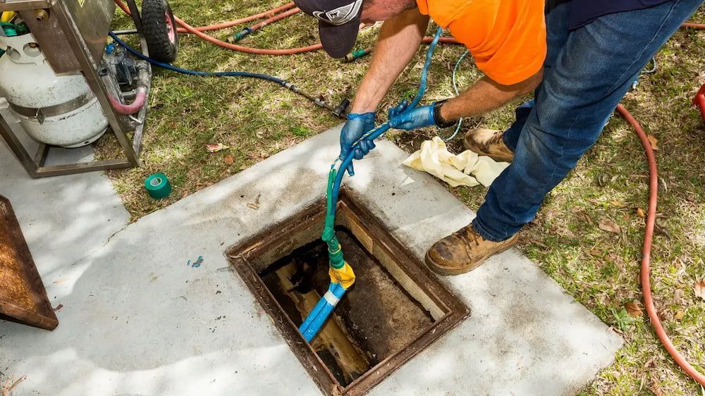 A Man is Cleaning a Manhole Cover With a Hose — FlowWise in Maroochydore, QLD