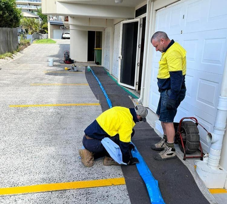 Two Men Are Working on a Blue Pipe in a Parking Lot — FlowWise in Maroochydore, QLD