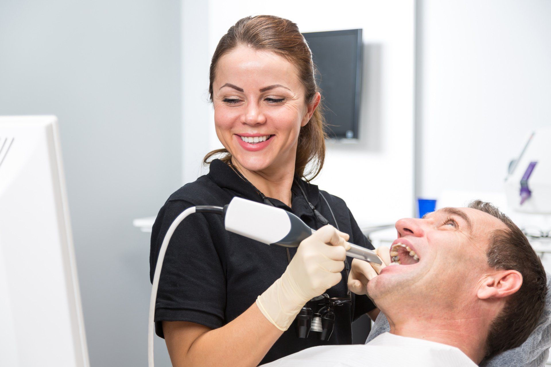 a female dentist is smiling while examining a man 's teeth with scanner