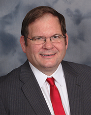Man in suit with glasses and red tie smiles.