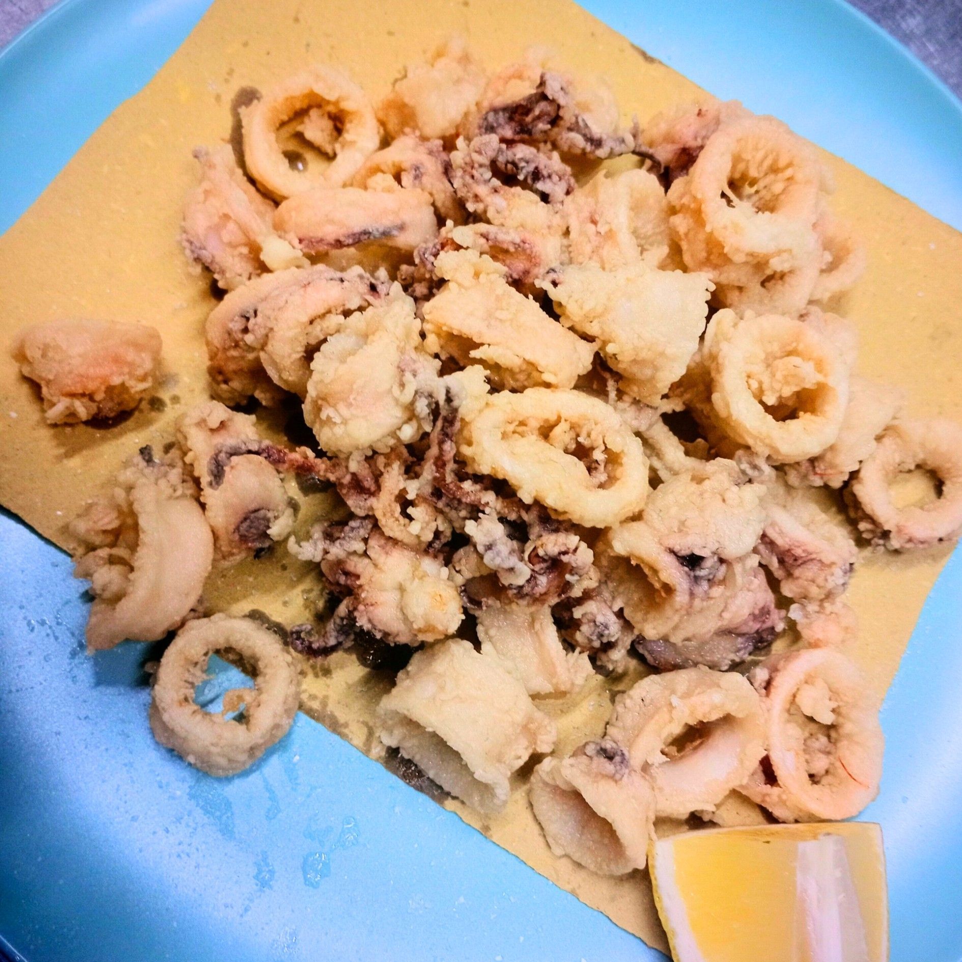 Un piatto blu con calamari fritti e una fetta di limone