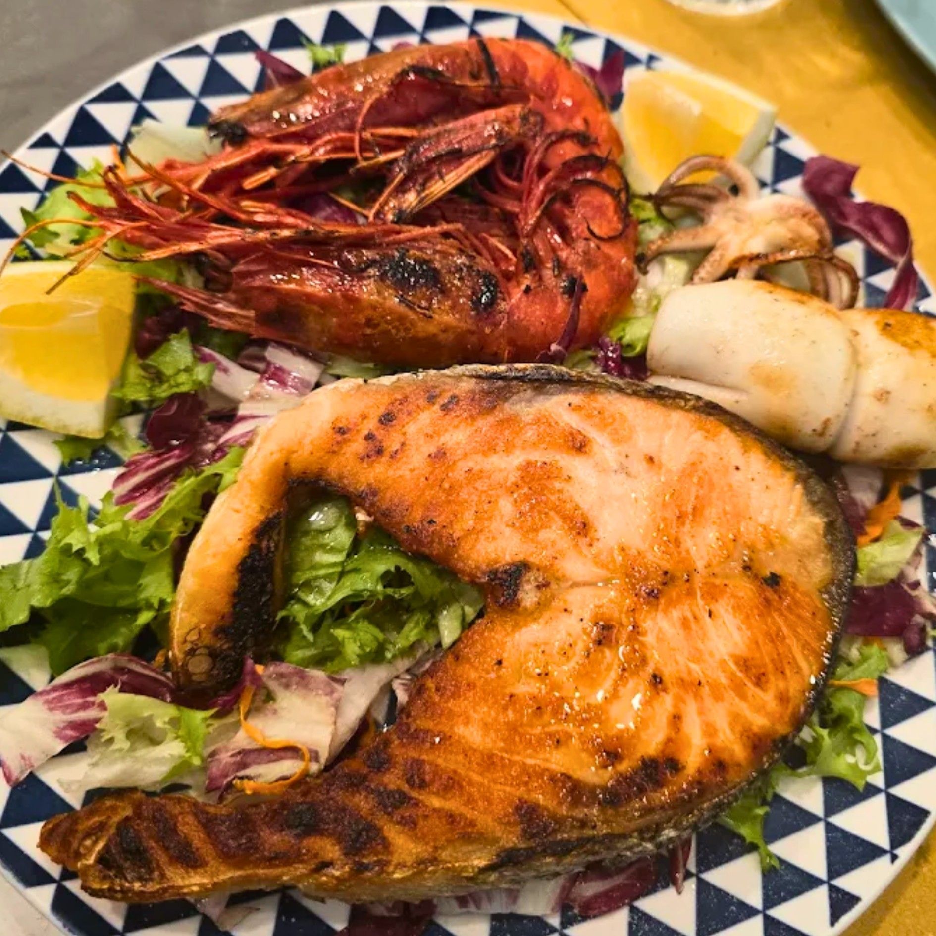 Un piatto di cibo con salmone, gamberi, calamari e lattuga su un tavolo.