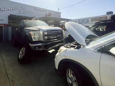 A ford truck is parked next to a white car with its hood open | Liebsack Auto Services