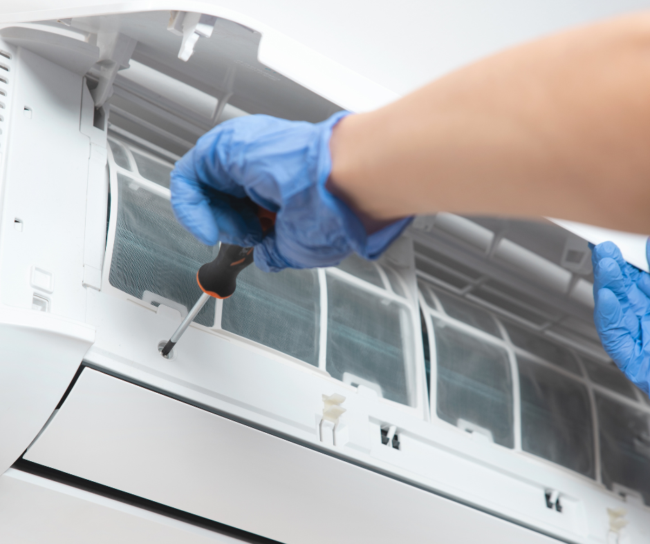 A person wearing blue gloves is working on an air conditioner