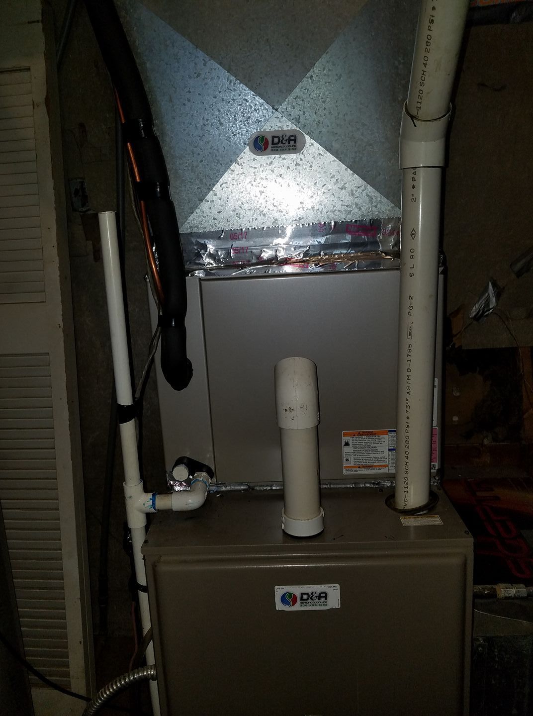 A furnace is sitting in a basement next to a pipe.