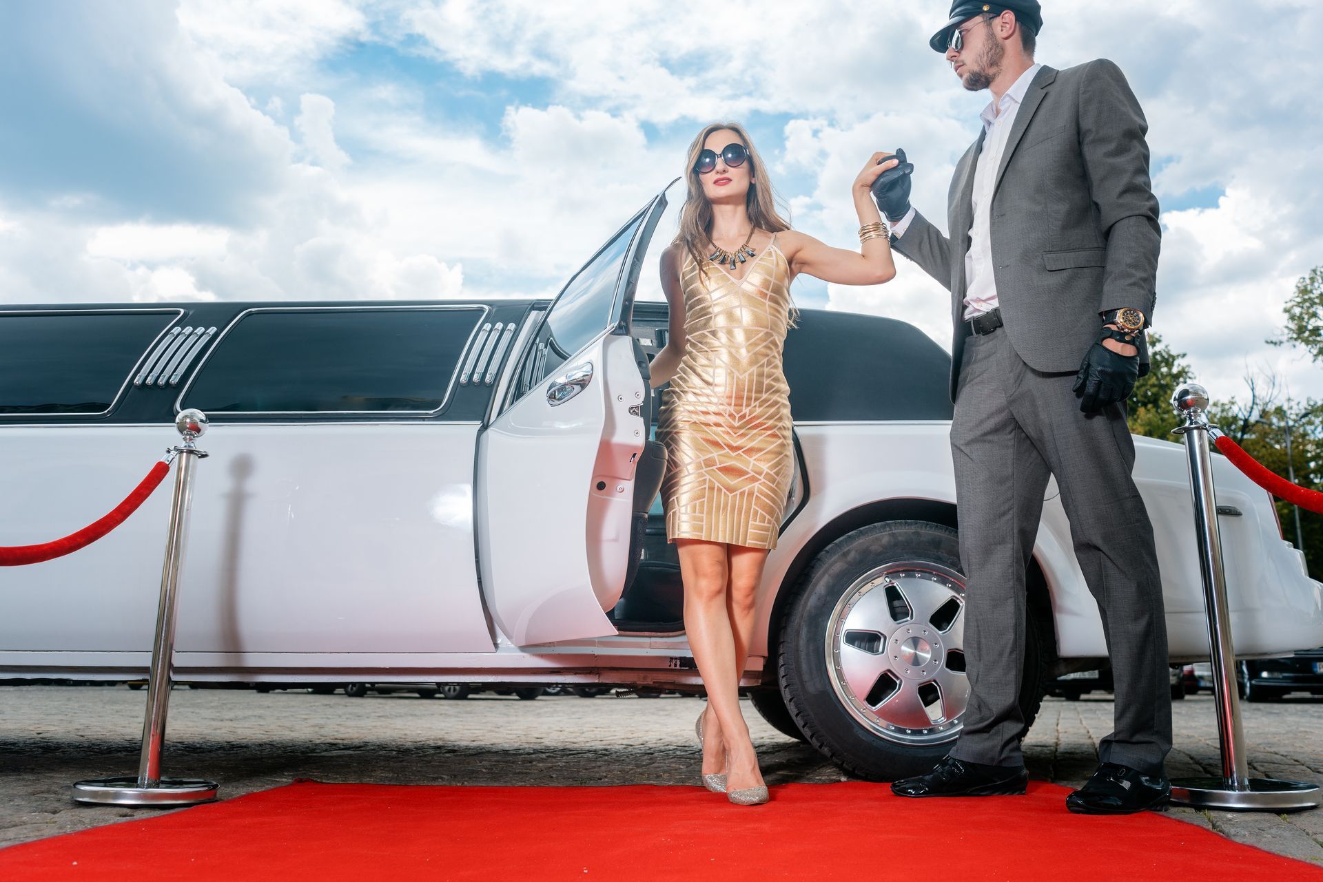 A man and a woman are standing next to a limousine on a red carpet.