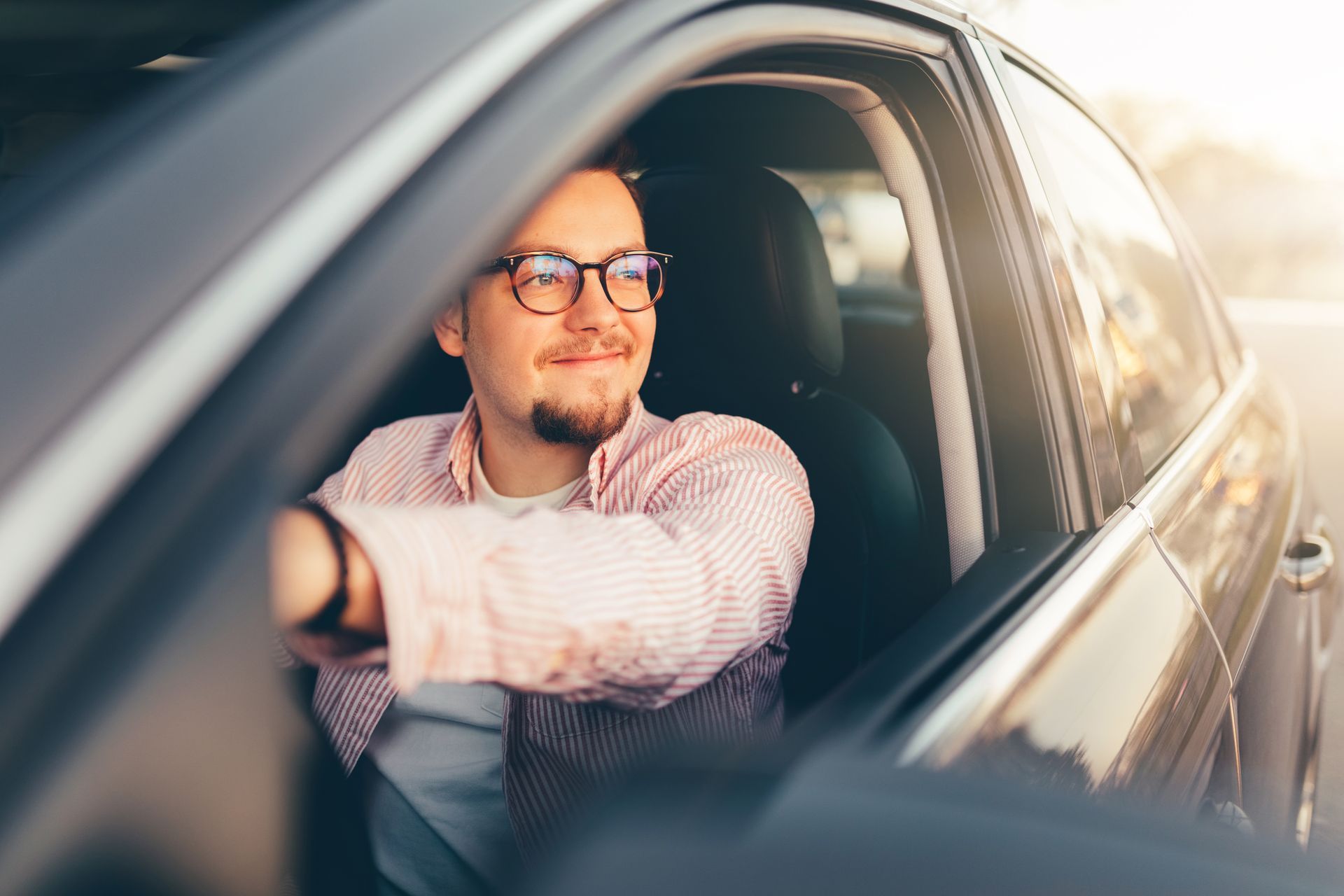 A man wearing glasses is sitting in the driver 's seat of a car.