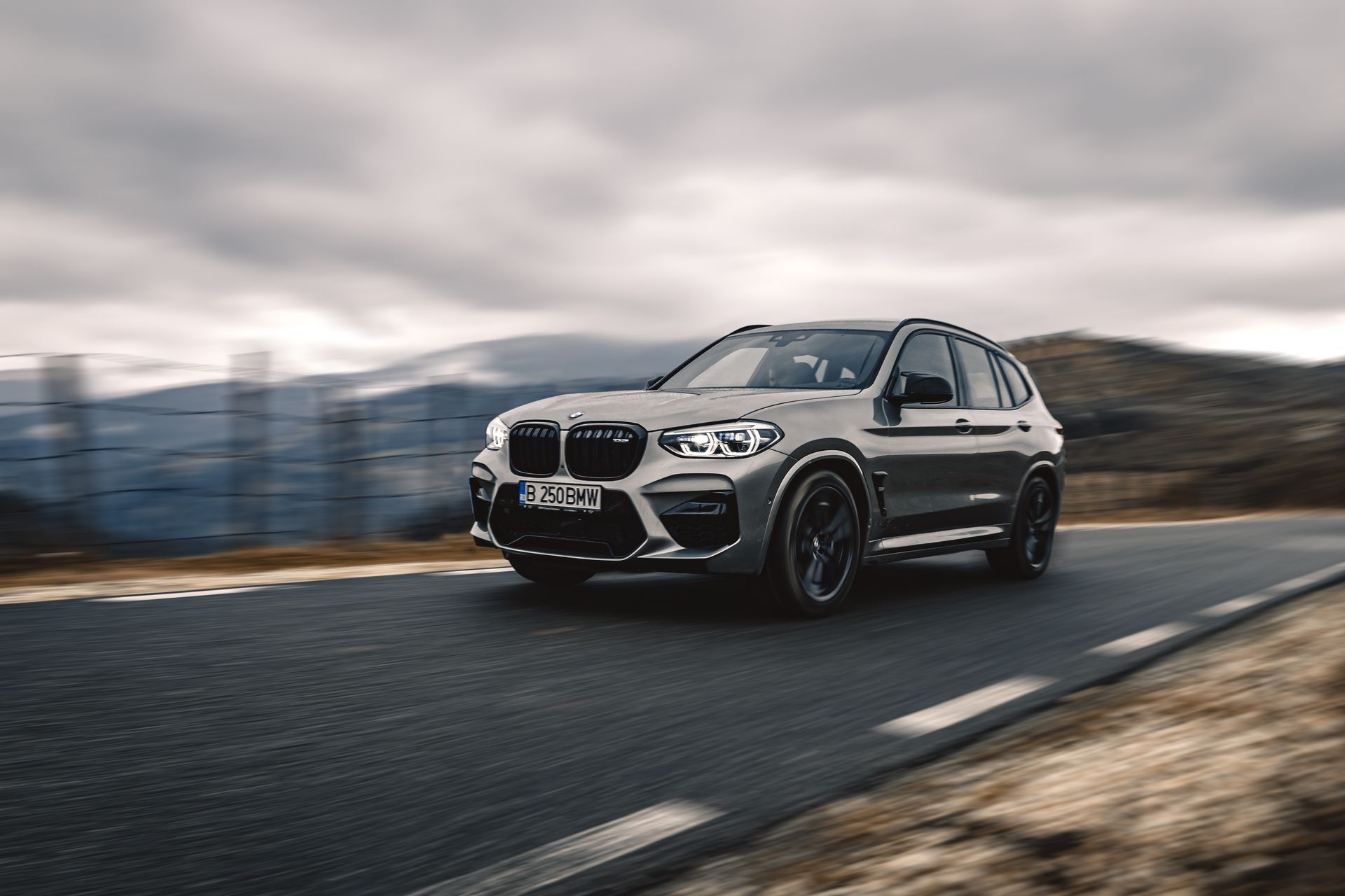 A white bmw x3 is driving down a mountain road.