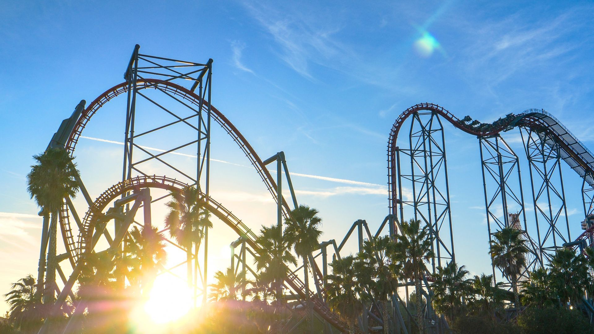 A roller coaster at an amusement park with the sun shining through the trees.