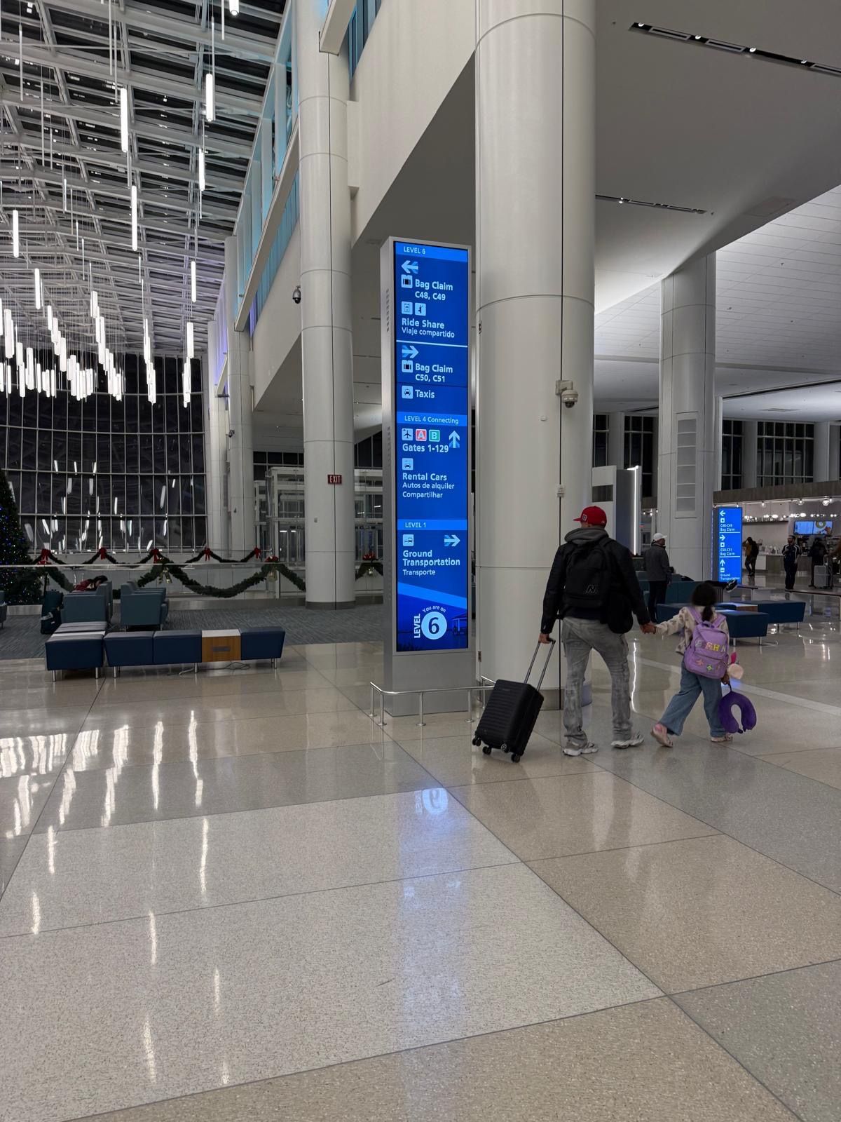 A man and a little girl are walking through an airport with luggage.