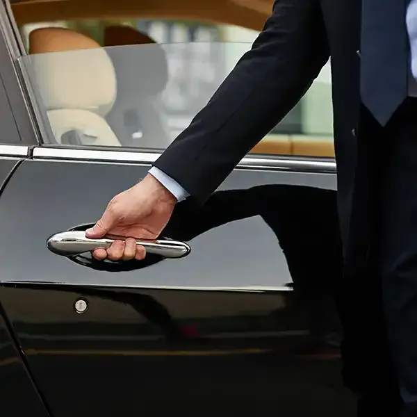 A man in a suit and tie is opening the door of a black car