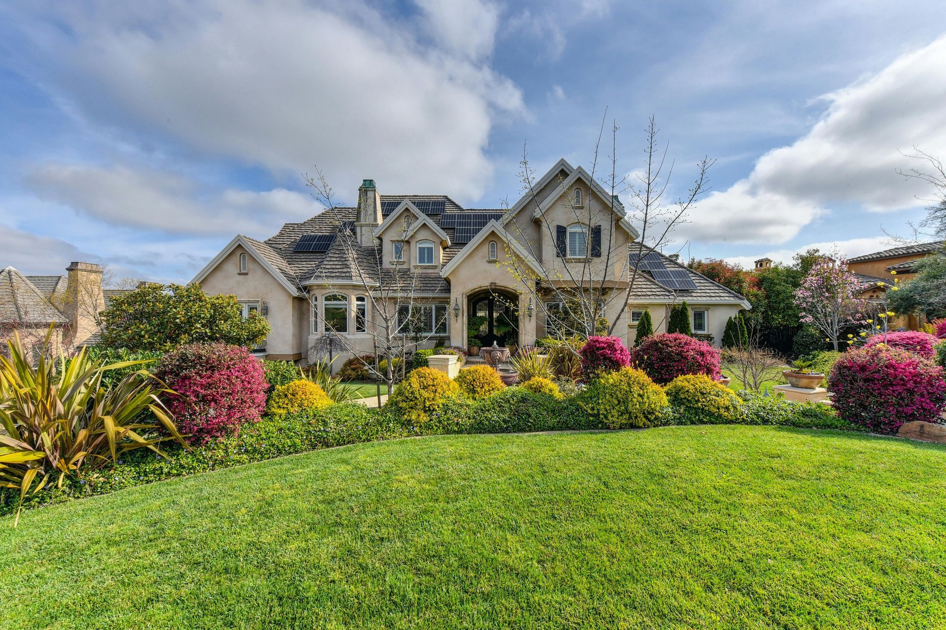 Elegant house with manicured lawn and vibrant flower beds under a cloudy sky.