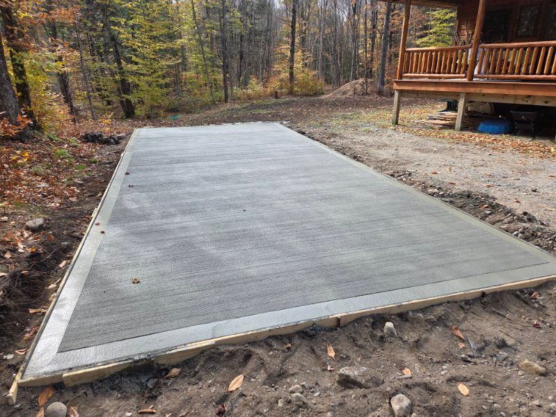 Newly poured rectangular concrete slab next to a wooden porch in a wooded area.