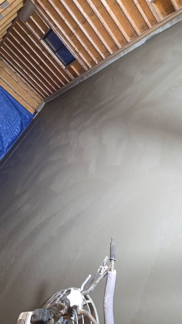 Interior wall with fresh plaster, under wooden rafters, blue tarp visible. A spray tool rests against the wall.