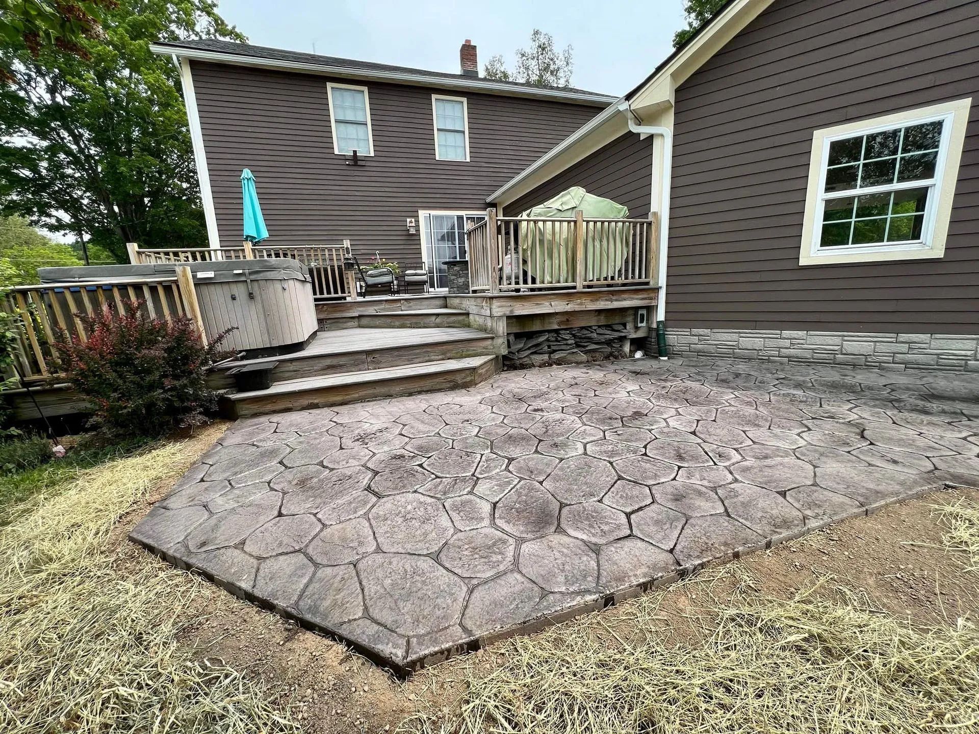 Backyard patio with stamped concrete, a wooden deck, and a brown house.