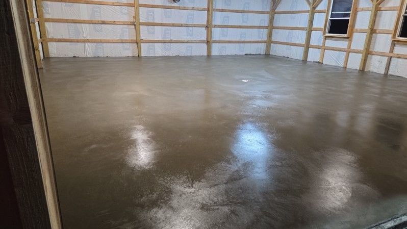 A freshly poured concrete floor inside a barn. Beige walls and wooden beams frame the room.