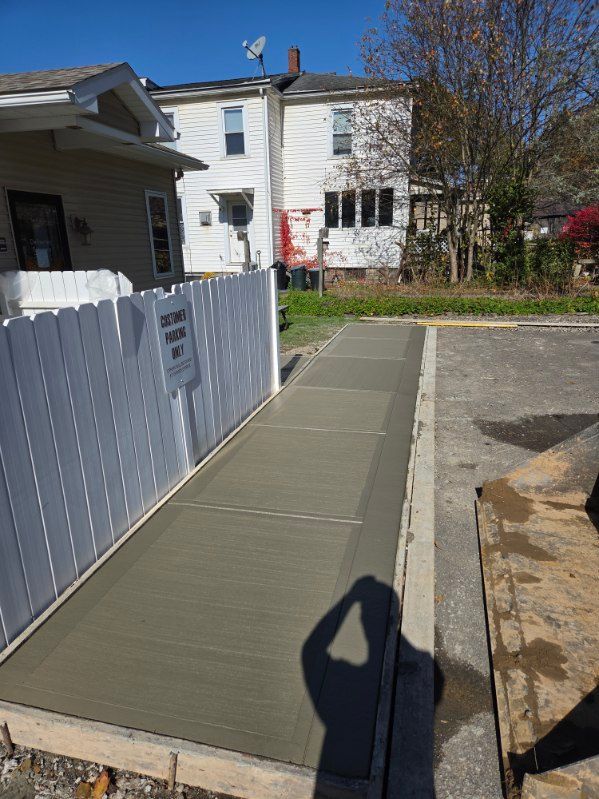 Freshly poured concrete ramp next to a white fence, leading towards a building. Bright sunny day.