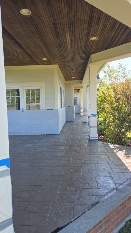 Covered porch with stamped concrete floor and wooden ceiling. White columns and light colored exterior walls.