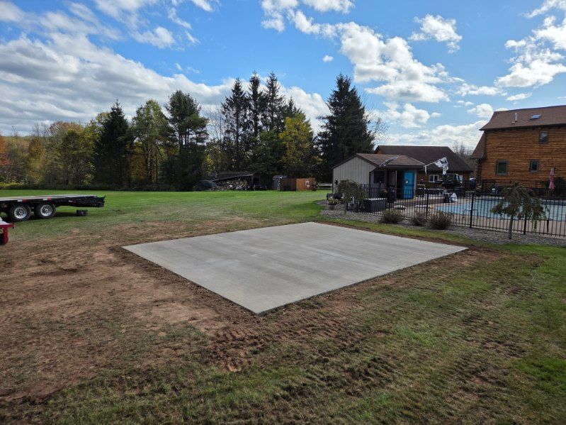 Concrete patio in a grassy yard, near a pool and a house, under a cloudy sky.