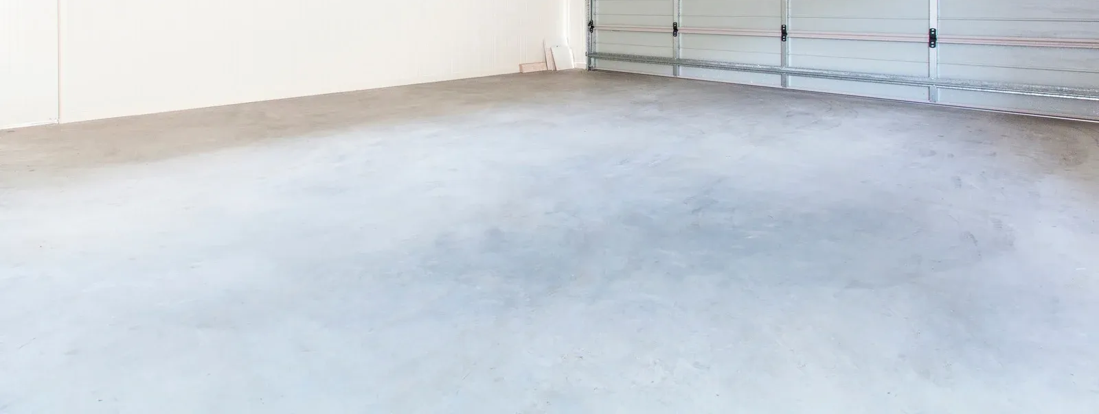 Concrete floor in an empty warehouse, with a white wall on the left and a closed garage door in the background.