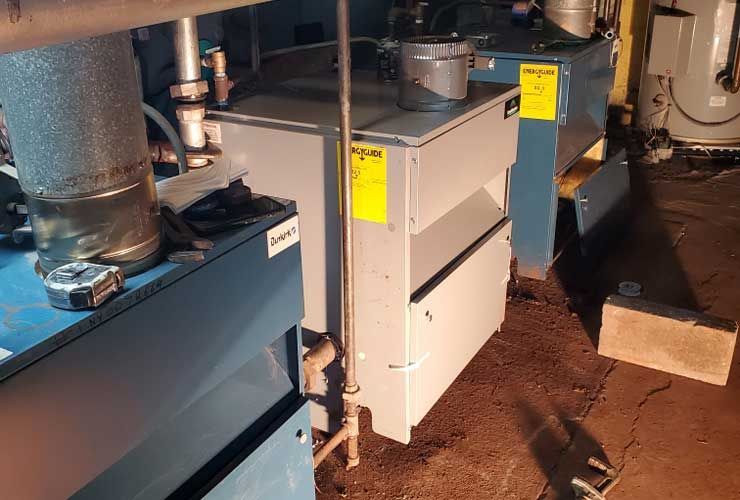 A boiler is sitting in a basement next to a pipe.