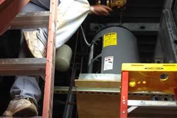 A man is working on a water heater while standing on a ladder.