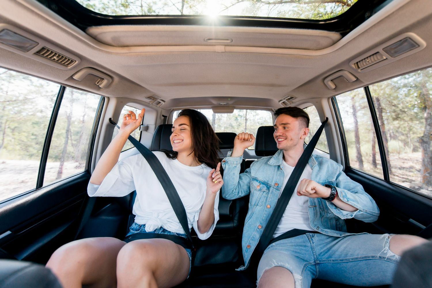 Young couple dancing and smiling in the backseat of a car with the sun shining through the sunroof.