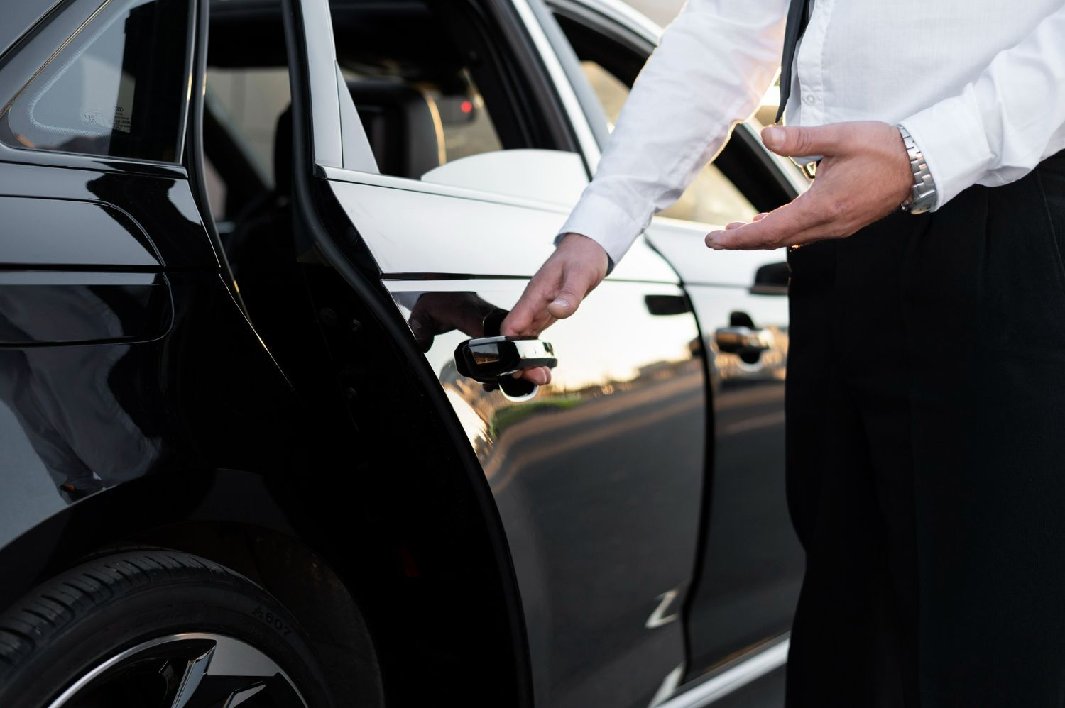 Man in formal attire opening a black car door.
