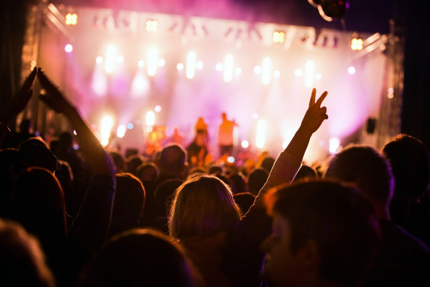 A crowd of people are watching a concert with their hands in the air.