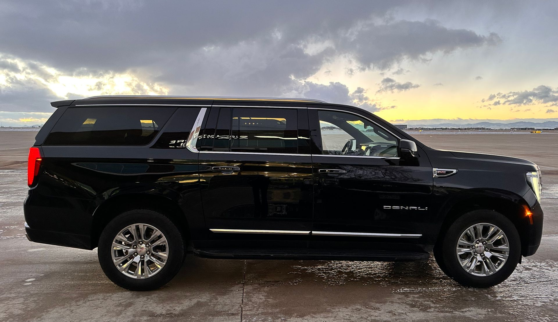 Black SUV parked at airport under a cloudy sky.