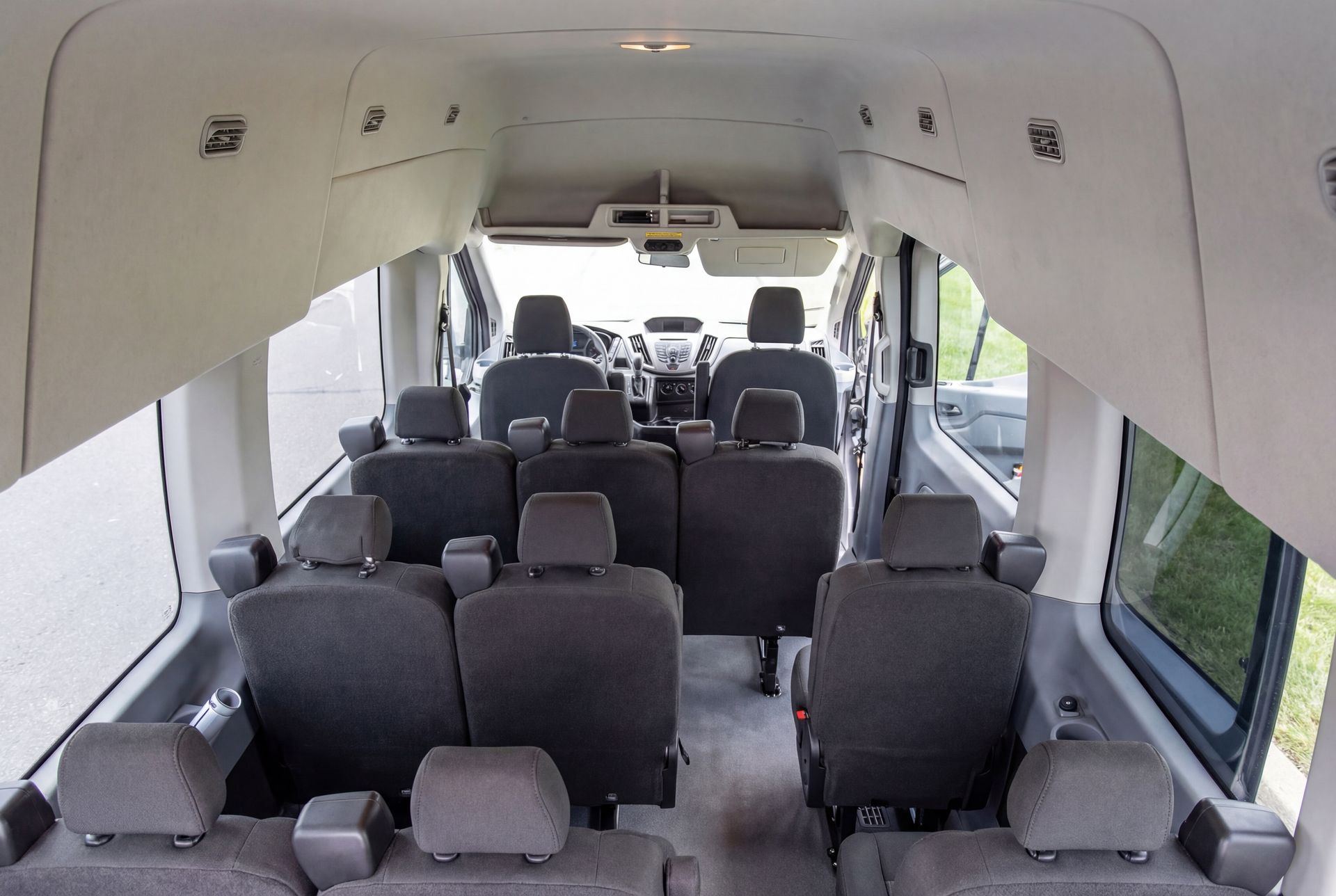 Interior of a passenger van with multiple gray seats. The front seats face the steering wheel. Windows are on the sides.